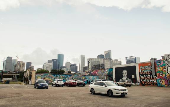 A diverse group of Texans using a car sharing service via smartphone app in an urban setting, with a modern car in the background. 
