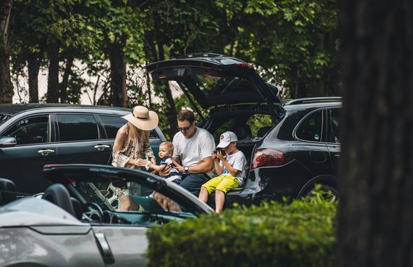 A Texas family standing by multiple cars in their driveway, reviewing car and home insurance documents together. Modern, friendly, and relatable. 